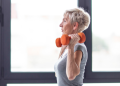 Mature woman lifts orange hand weights in a gym
