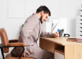 Man sitting at desk holding back in pain