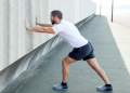 Man stretching his calves by pressing arms against wall of building