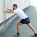 Man stretching his calves by pressing arms against wall of building