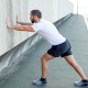 Man stretching his calves by pressing arms against wall of building
