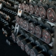 A perspective shot of a gym weight rack filled with multiple rows of black dumbbells. The weights feature red circular accents and numerical labels indicating their weight in kilograms. The rack recedes into the background, creating a sense of depth and variety, highlighting the range of equipment available for strength training.